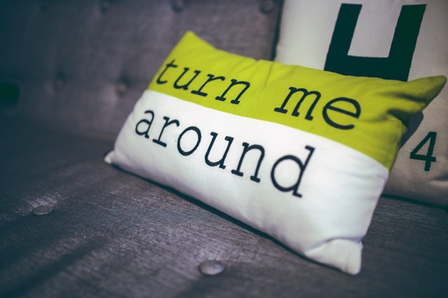 Bielo-zelený vankúš s nápisom turn me around na posteli